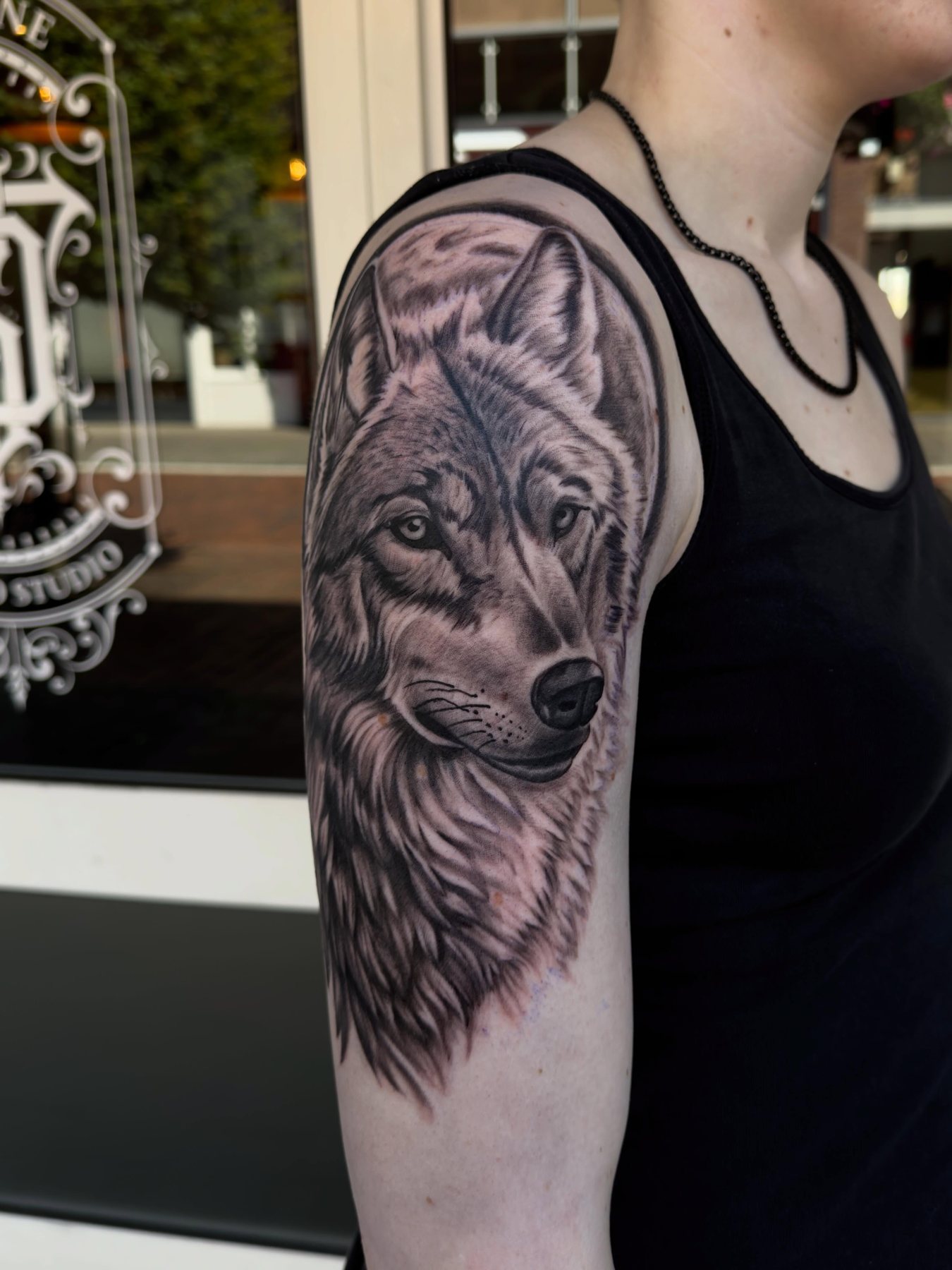 Wolf in black & grey op een bovenarm, met het Darkline-logo op het raam van de studio erachter