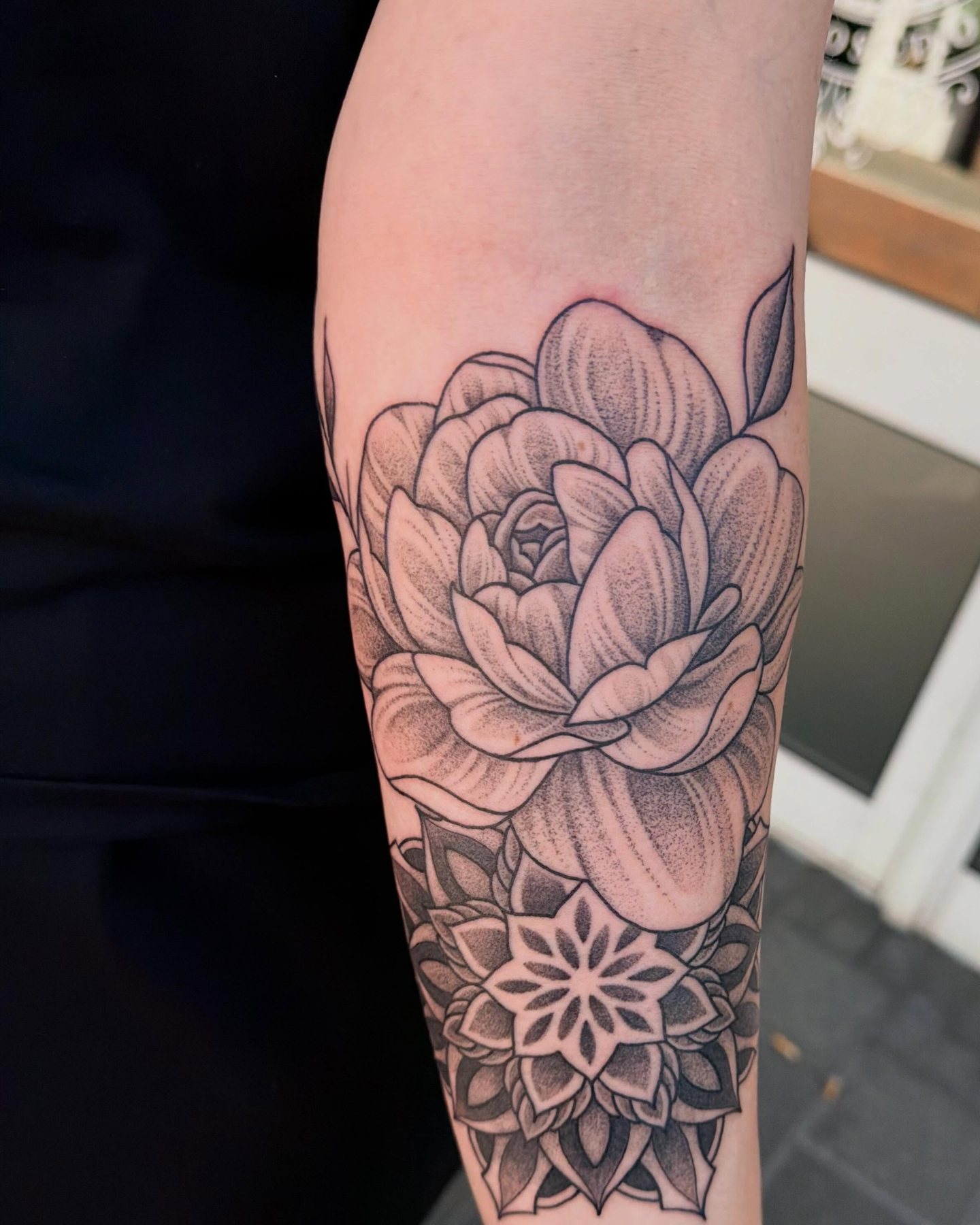 Pioenroos met een mandala eronder op een onderarm